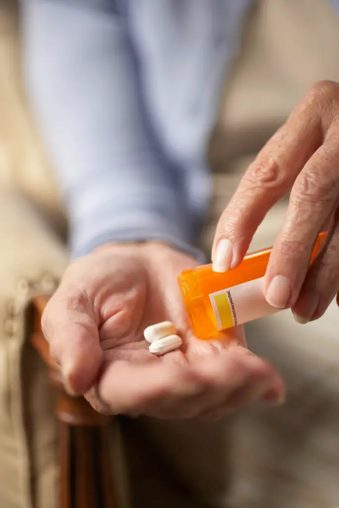 Senior woman tipping pills from prescription bottle, close-up of hands