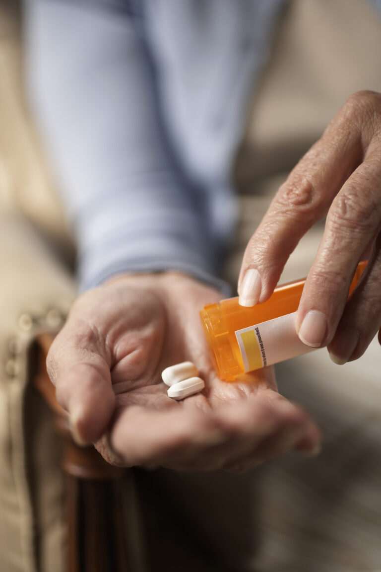 Senior woman tipping pills from prescription bottle, close-up of hands