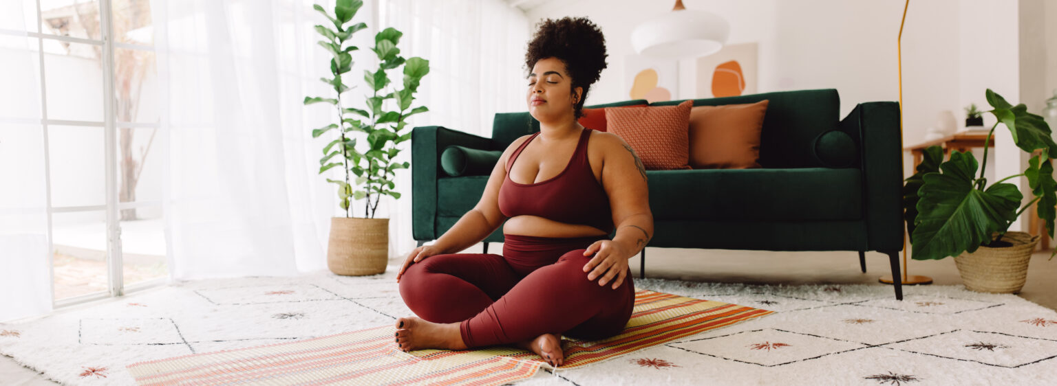 Woman sitting cross legged and closed eyes in living room, practicing meditation.