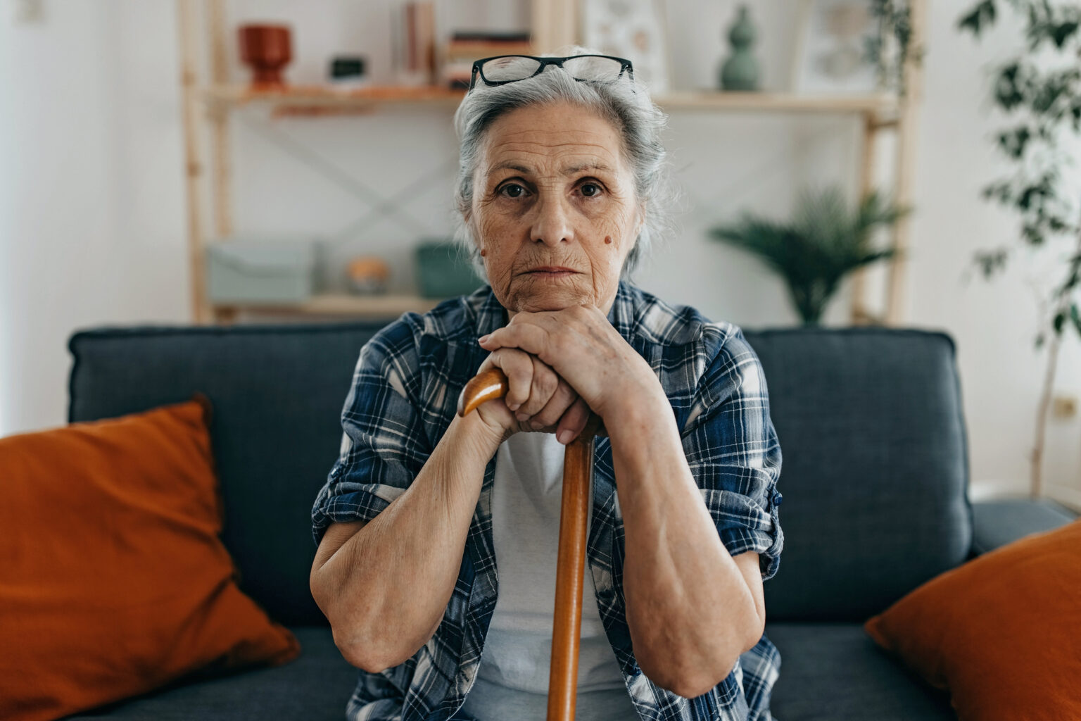 Tired older woman sitting on sofa, holding a walking stick