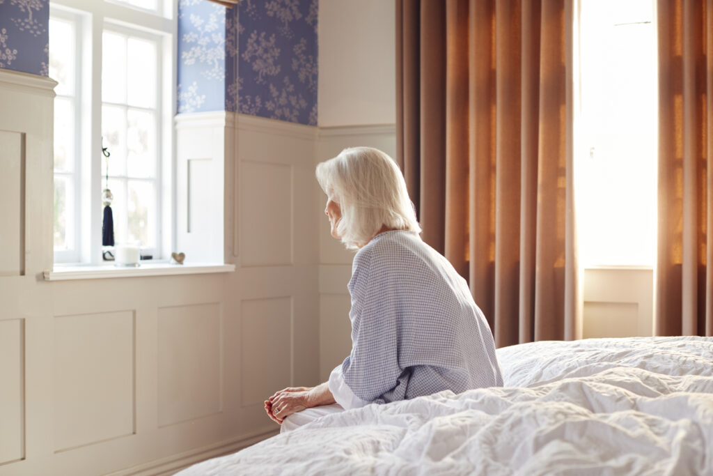 Unhappy And Anxious Senior Woman Sitting On Edge Of Bed At Home