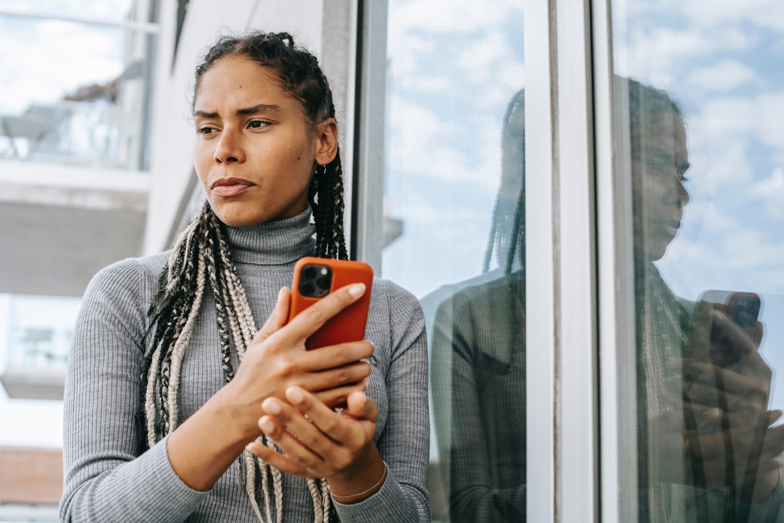 African American woman stands near window, holding smart phone in hands