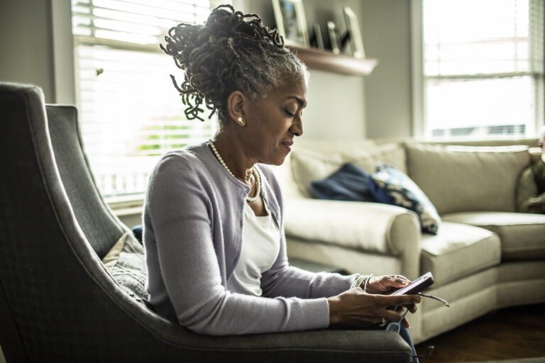 Senior woman using smartphone in living room of suburban home