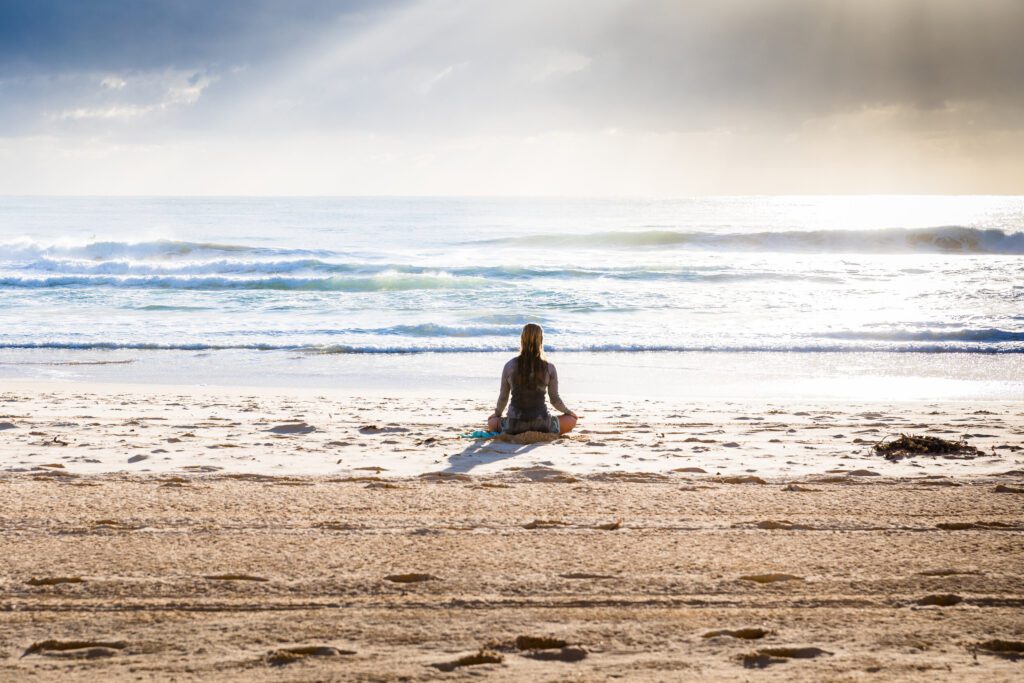 photo of woman meditating on a beach, waves crashing in background