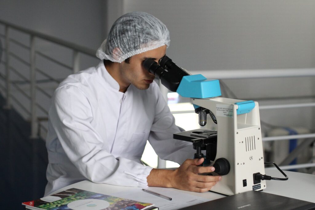 Photo of a male researcher dressed in white, looking into a microscope