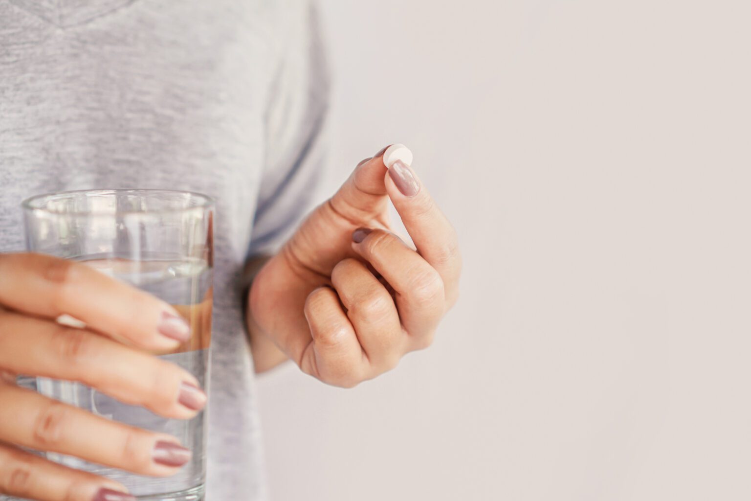 closeup woman hand taking pill with glass of water