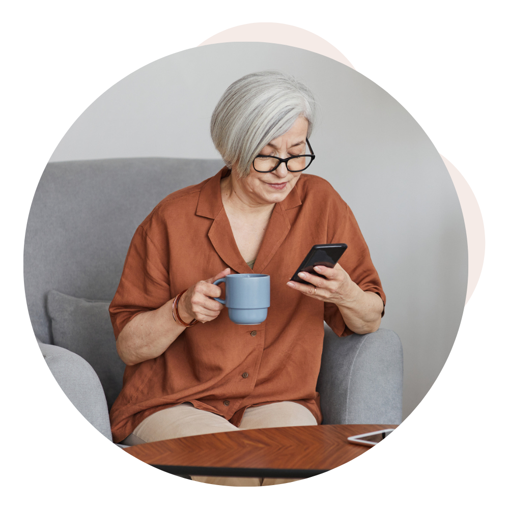 woman sitting on couch, reading cellphone, and drinking tea