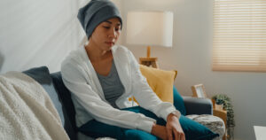 Young Asian woman sick with cancer sitting on sofa in living room at home. Healthcare concept.