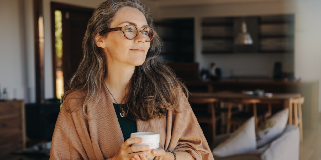 mature woman holding a coffee cup, standing in her kitchen at home