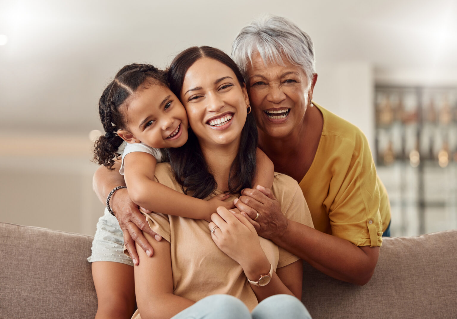 Grandmother, mom and child hug in a portrait for mothers day on a house sofa as a happy family in Colombia. Smile, mama and elderly woman love hugging young girl or kid and enjoying quality time