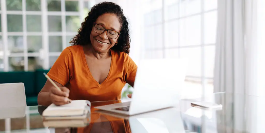 Happy senior woman sitting at a table in her home office, writing in a journal.