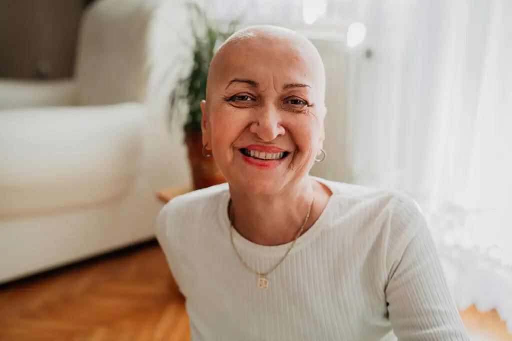 Woman sitting on a wood floor in a white sweater smiling at the camera