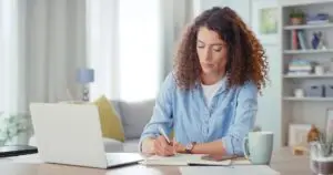 woman making an appointment on her computer and writing it down at home