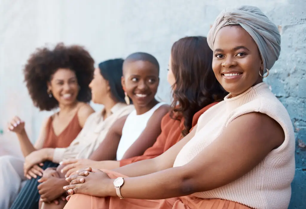 Young Black businesswoman sitting in a line with her coworkers against a wall outside in the city.
