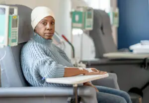 An older woman wearing a head scarf sits patiently as she receives her IV drip.