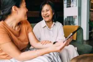 Young woman and her mother looking at the photographs on the tablet device. They are comfortably sitting on the sofa in the living room at their home, casually talking and enjoying their time together.