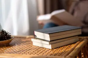 Closeup image of books on wooden table with blurred person reading book in background
