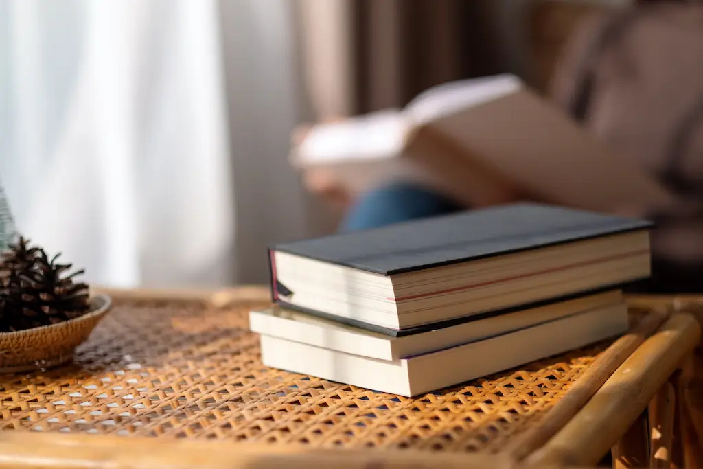 Closeup image of books on wooden table with blurred person reading book in background