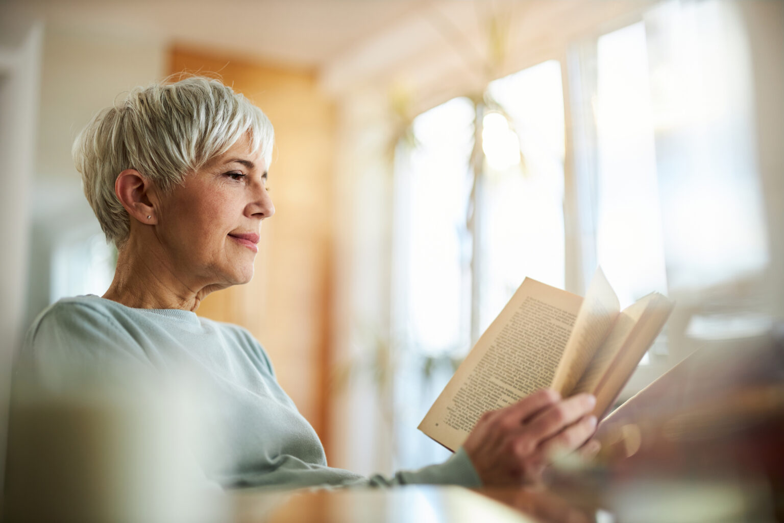 older woman sitting at a desk reading a book at home