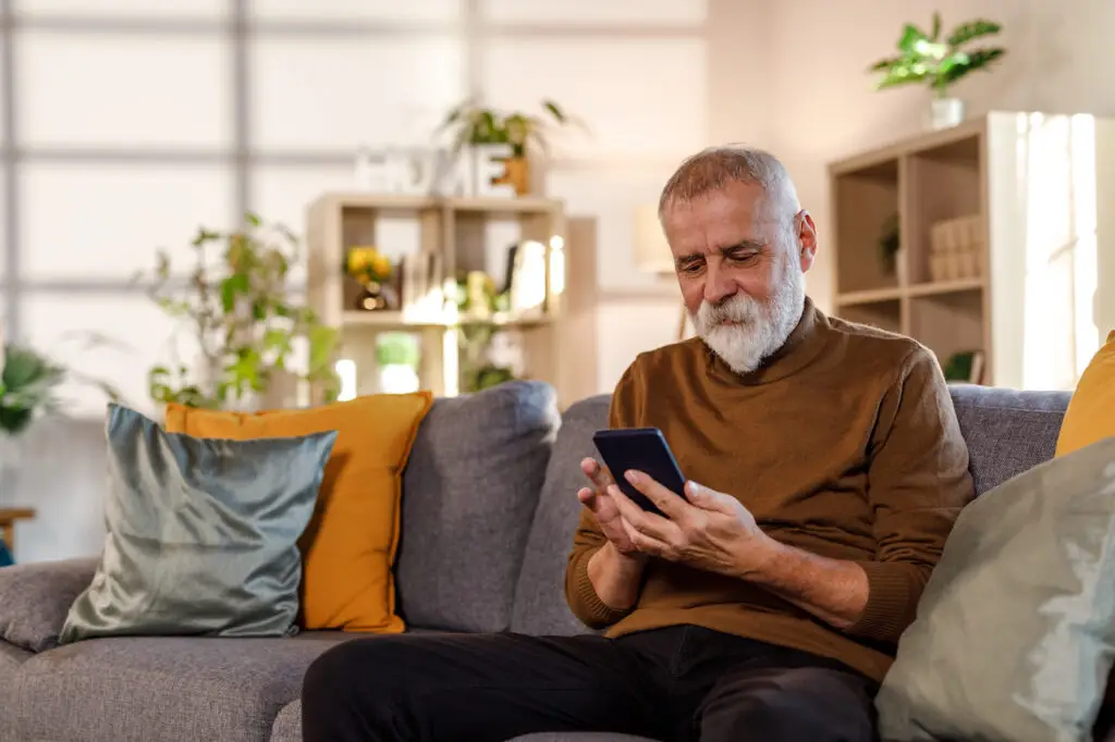 Mature man sitting on the sofa, using his smart phone