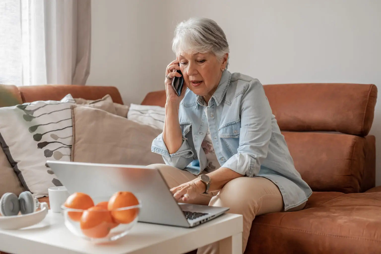 older woman at home talking on the phone with her laptop open