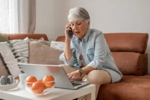 older woman at home talking on the phone with her laptop open