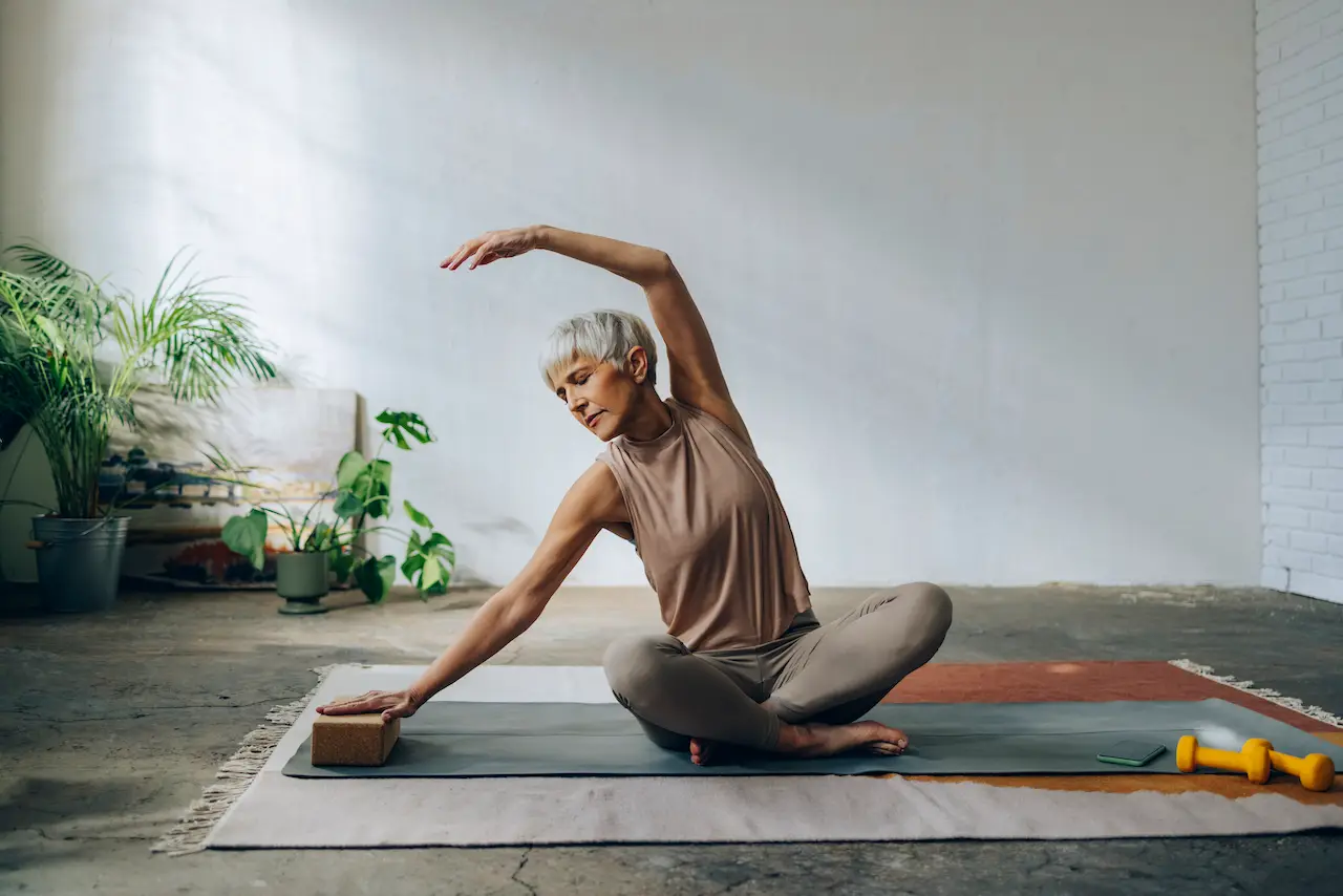 woman in sportswear sitting on a exercise mat and stretching arms.