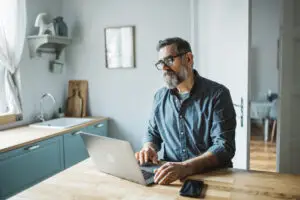 older man working on computer in kitchen at home