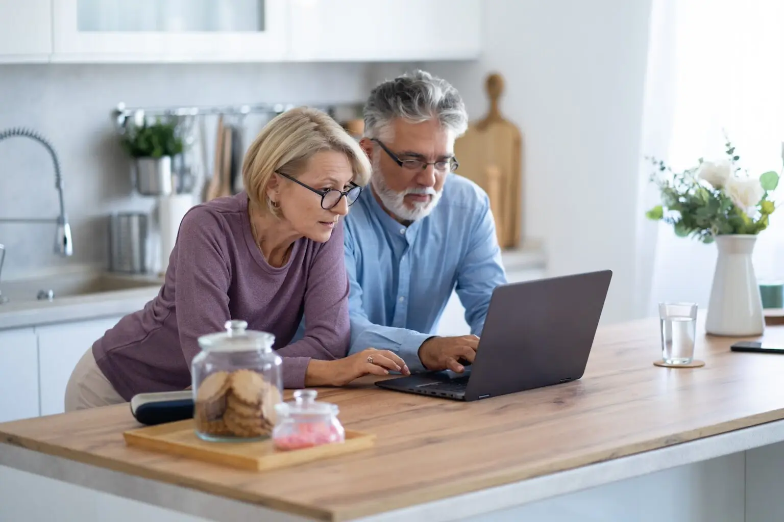 senior couple in the kitchen looking at a laptop together