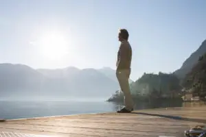 Man stands on edge of pier over a lake at sunrise