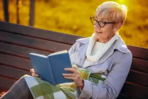 older woman reading book on bench outside