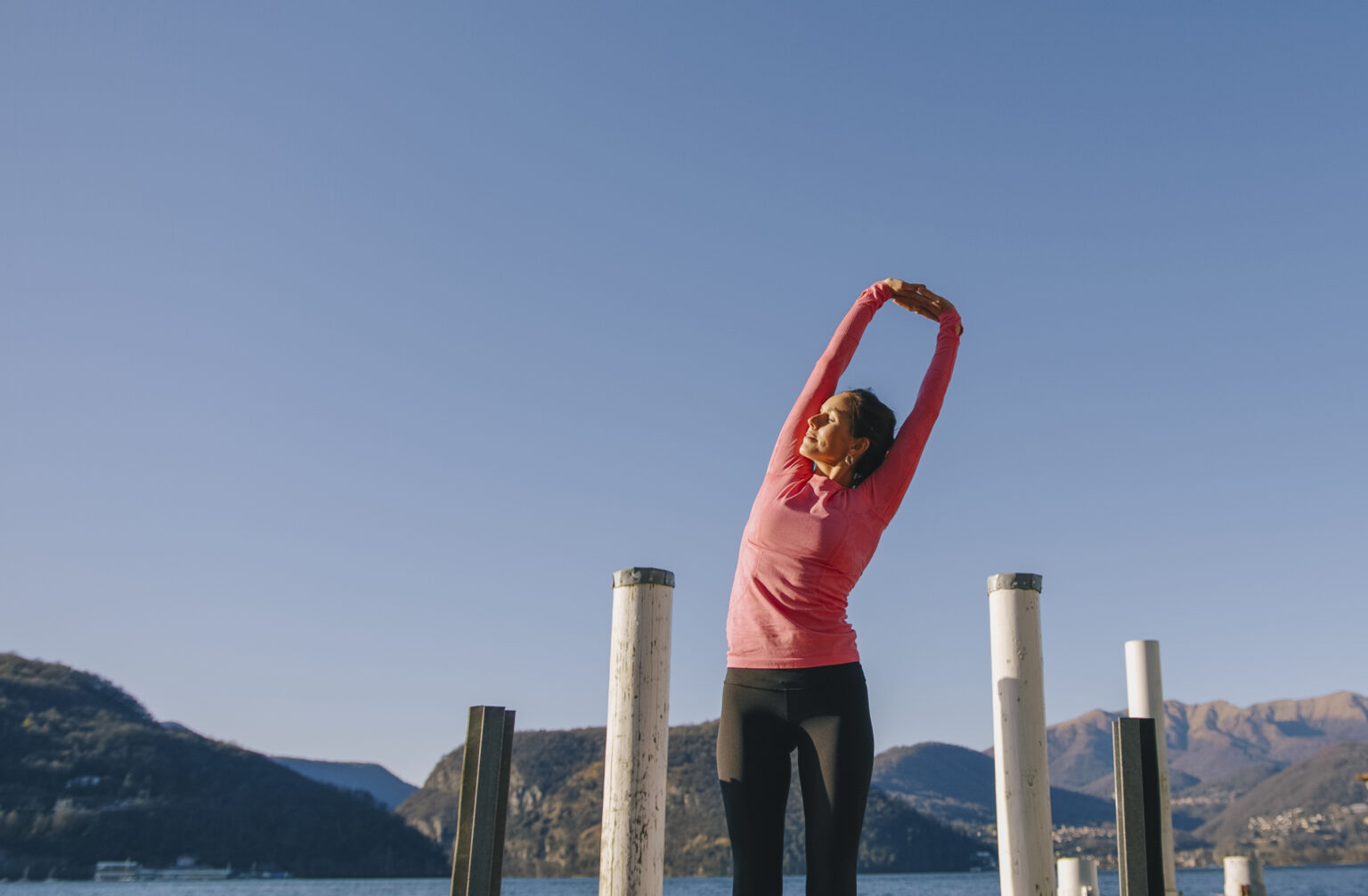 Woman performs yoga moves on lakeside pier