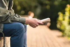 close up of a man sitting in a park reading a book