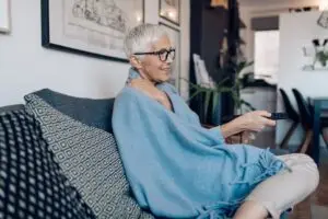 Senior woman enjoying at her living room, watching TV.