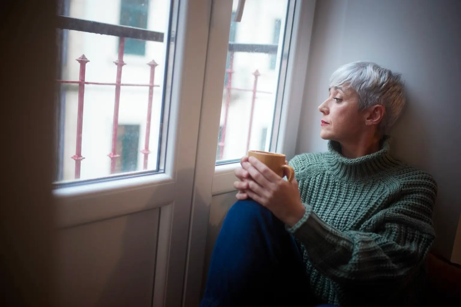 Close-up of senior woman sitting by the window drinking coffee