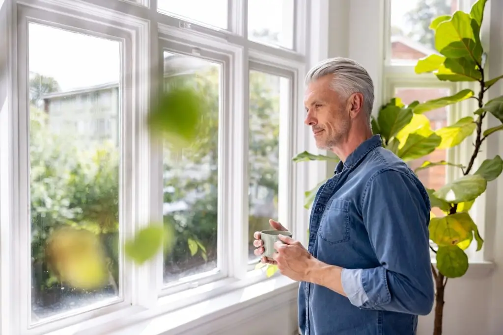 older man with a mug looking at the window at home