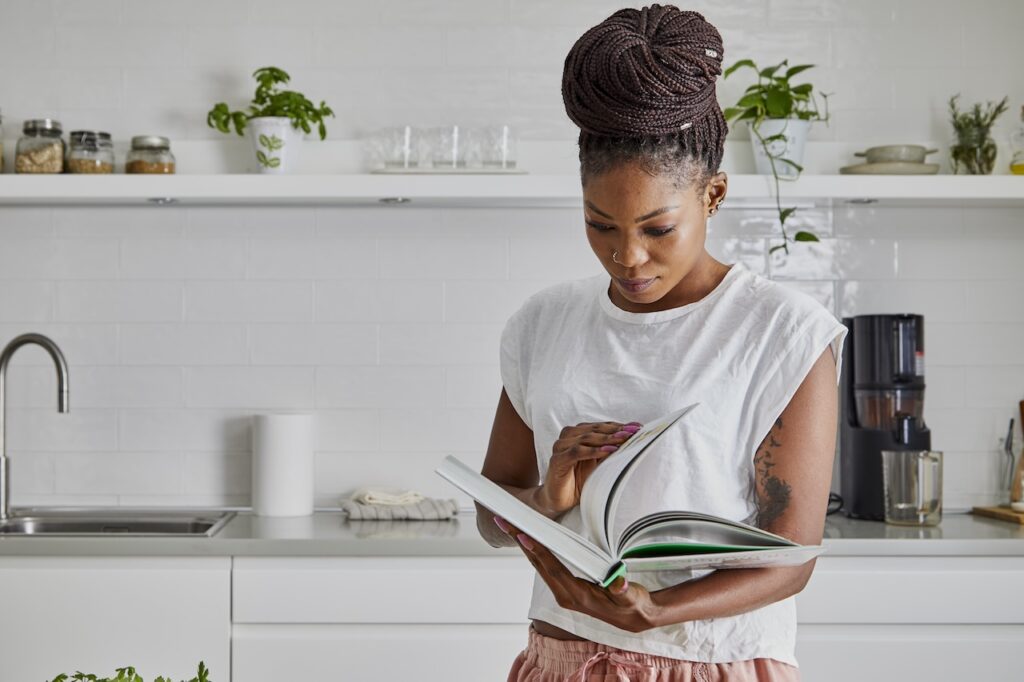 woman reading a cookbook in the kitchen standing