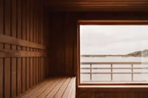 The inside of an empty dry sauna with large windows. Walls and benches made of wood and a tile floor