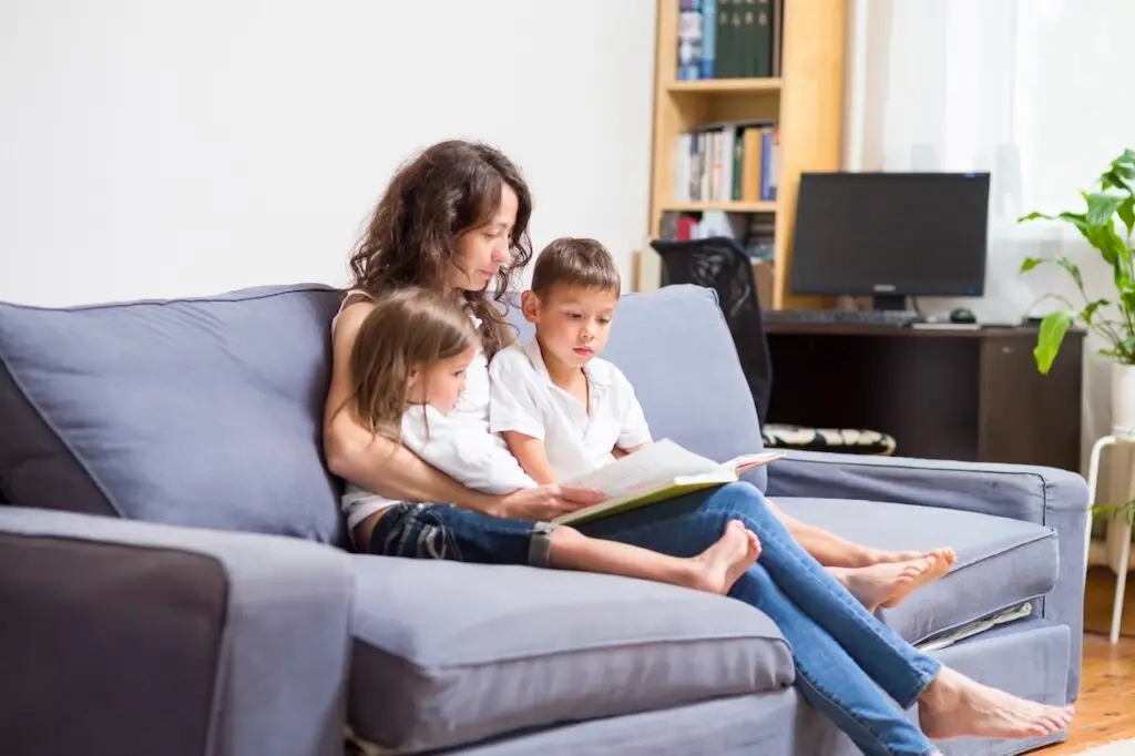 a mother reading a book to children on the couch