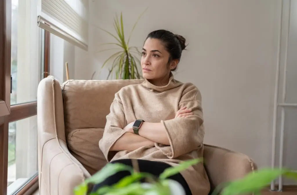 Woman Sitting On Armchair By Window And Looking Outside Through Window At Home