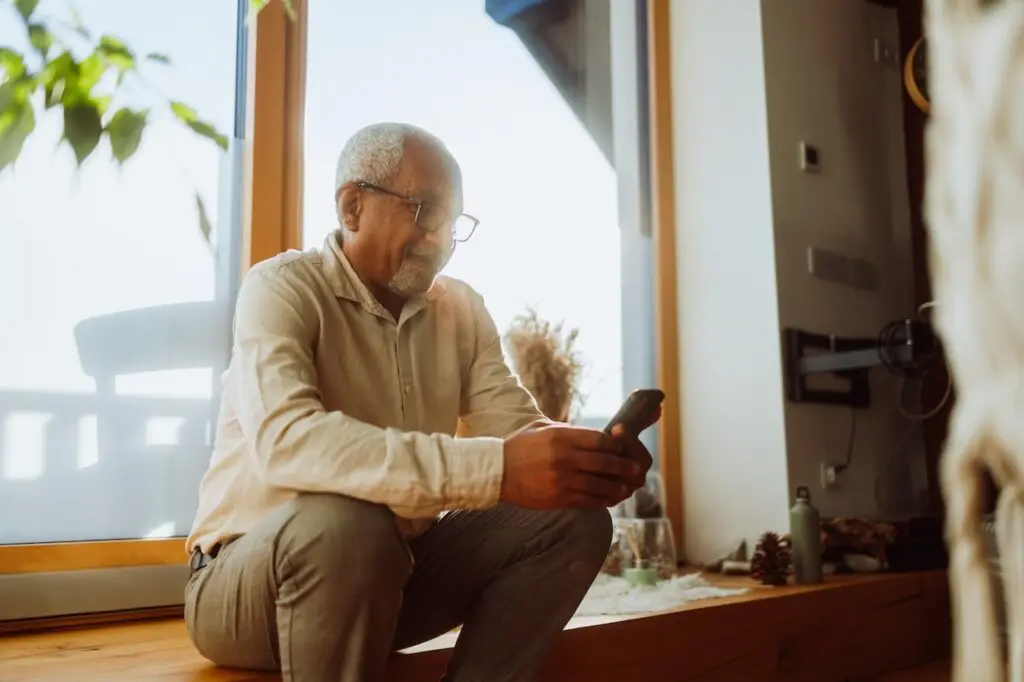 older man using phone next to window sitting down