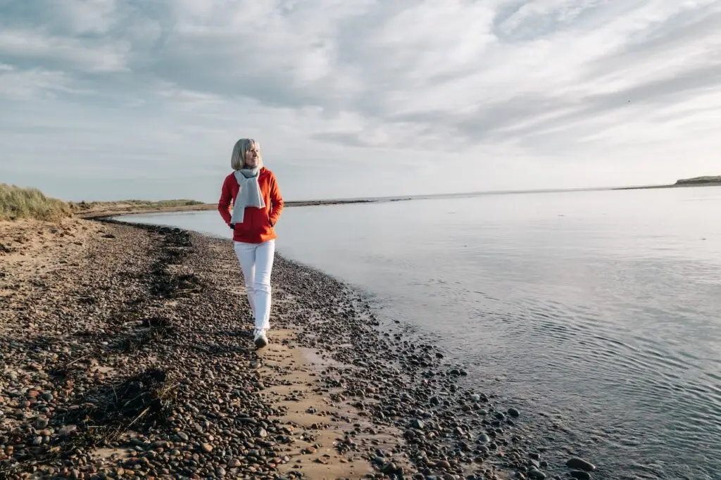 older woman walking along a lake smiling
