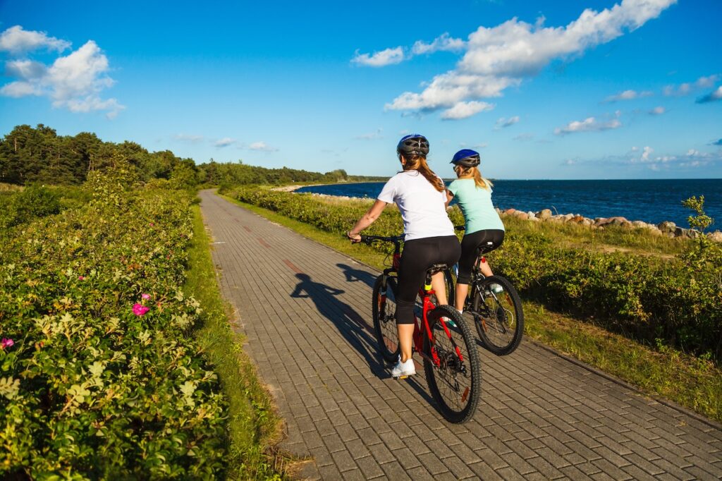 women riding bikes on bike path next to ocean