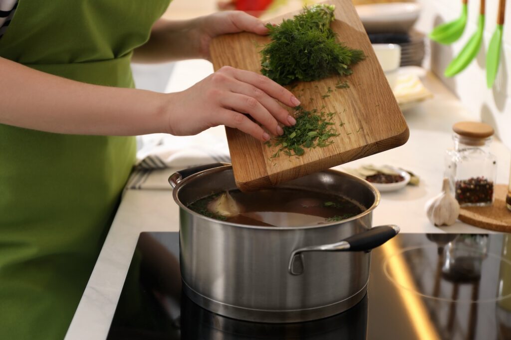 woman putting dill into a pot of broth on stove