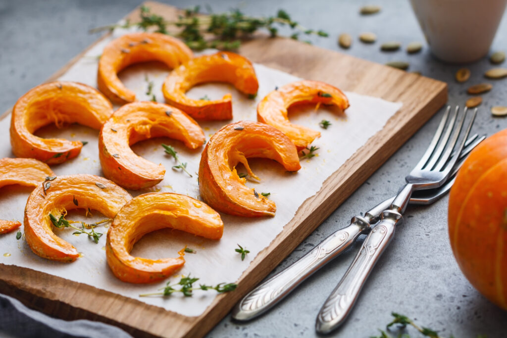 Baked pumpkin slices with thyme on a wooden board over grey table.