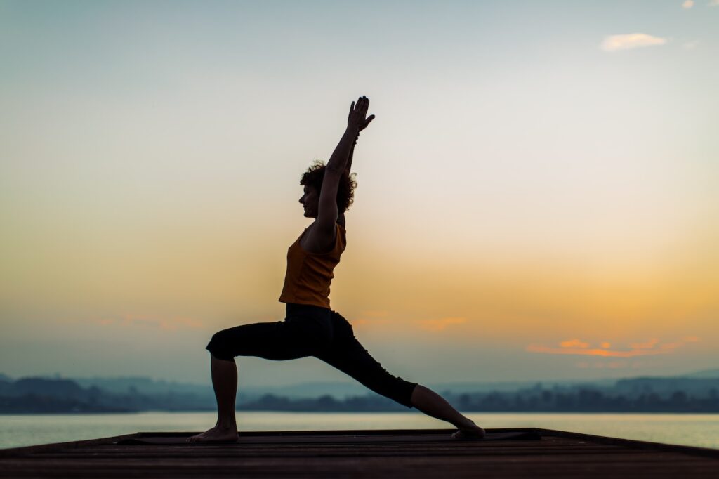 Woman doing yoga near lake at sunset