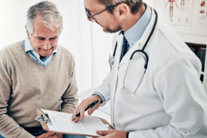 Male doctor and patient in exam room reading treatment plan.