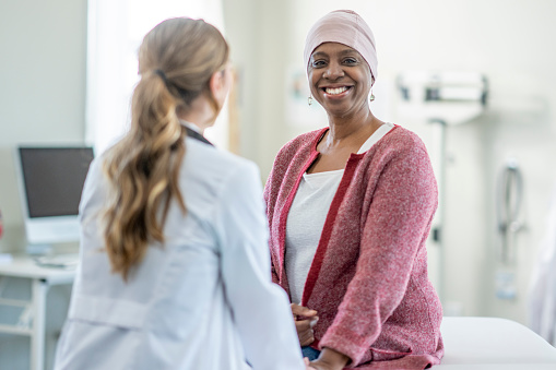 A female doctor sits across from her cancer patient of African decent, as they talk about her treatment plan and recent side effects.