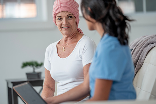 A caring nurse engages with a patient wearing a headscarf, promoting comfort, empathy, and understanding in a cozy living space.