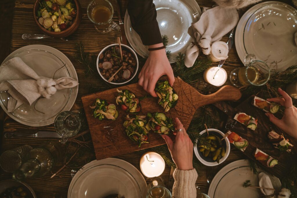 Family sharing a festive meal at dinner table. Two individuals are reaching for food in the middle of table.